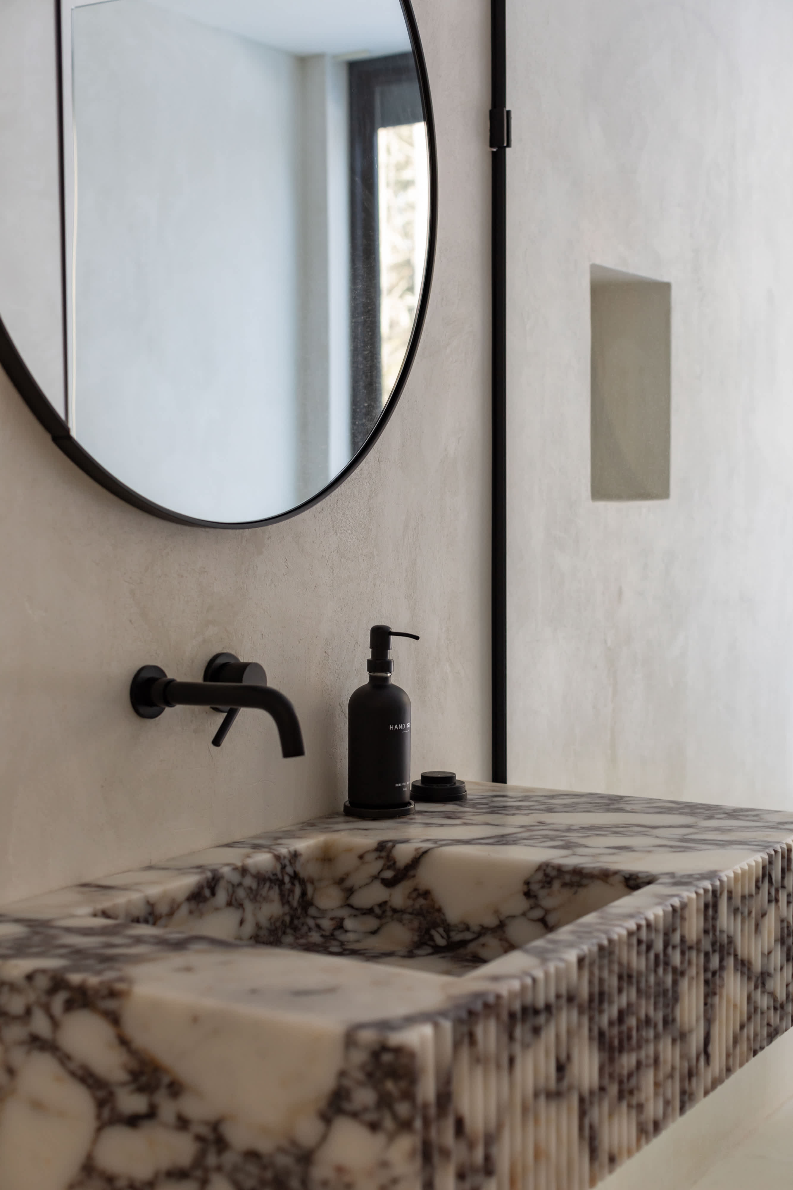 Stylish bathroom vanity featuring a black-veined marble countertop and integrated sink with a fluted front, complemented by a round black-framed mirror and modern black wall-mounted faucet.