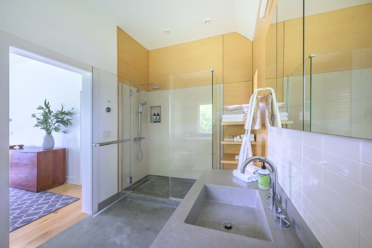 Modern bathroom with light wood paneling, a glass-enclosed walk-in shower, a concrete-look vanity with an integrated sink, and white subway tile backsplash.