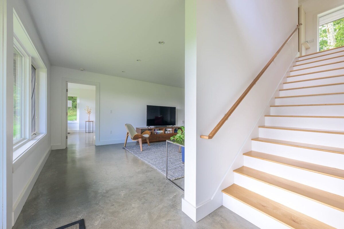 Open concept living space with polished concrete floors, a modern staircase with white risers and wood treads, and a living area featuring a large TV on a wooden console.
