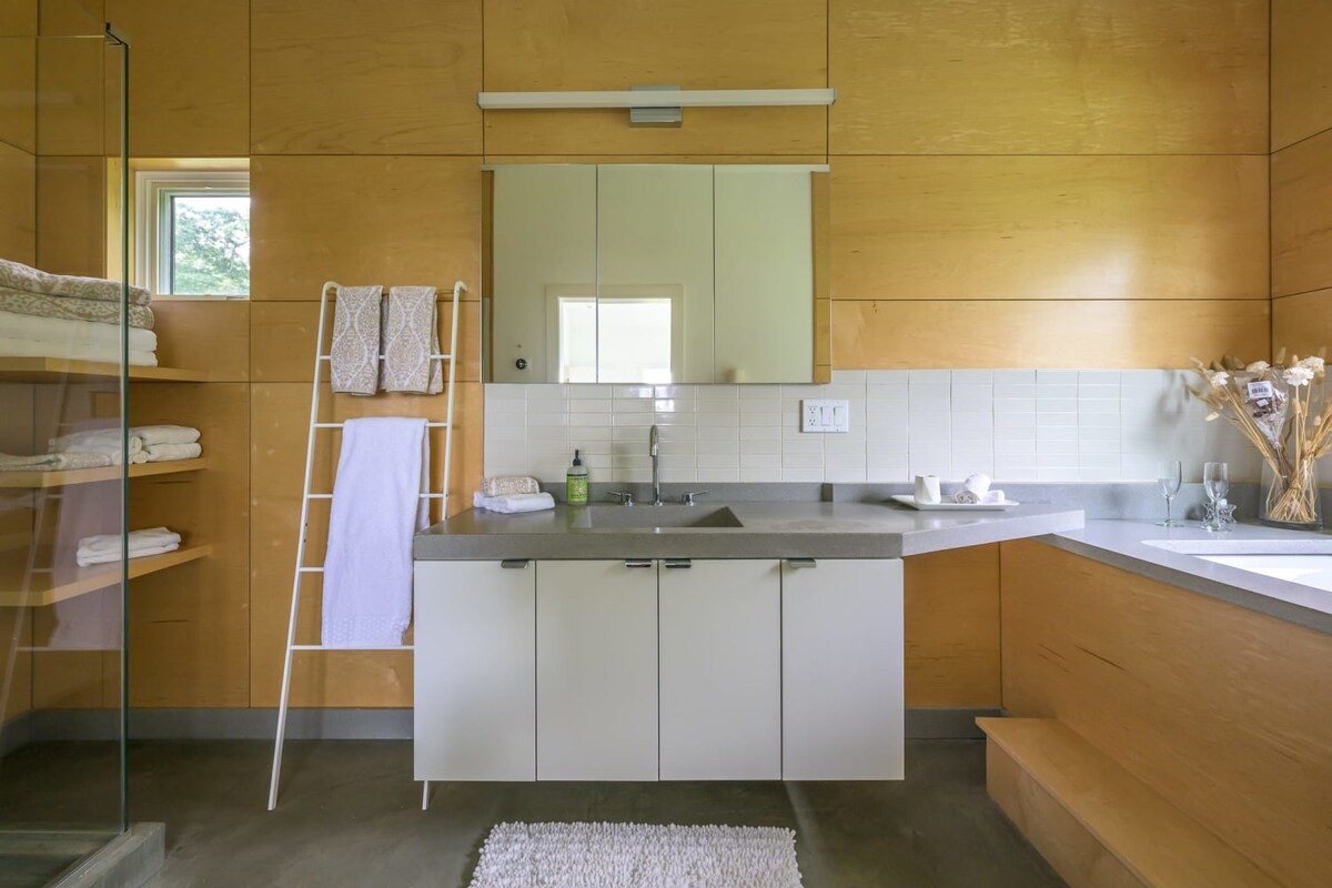 Contemporary bathroom featuring light wood paneling, a concrete-look countertop with an integrated sink, white flat-panel vanity cabinets, and a white ladder-style towel rack.
