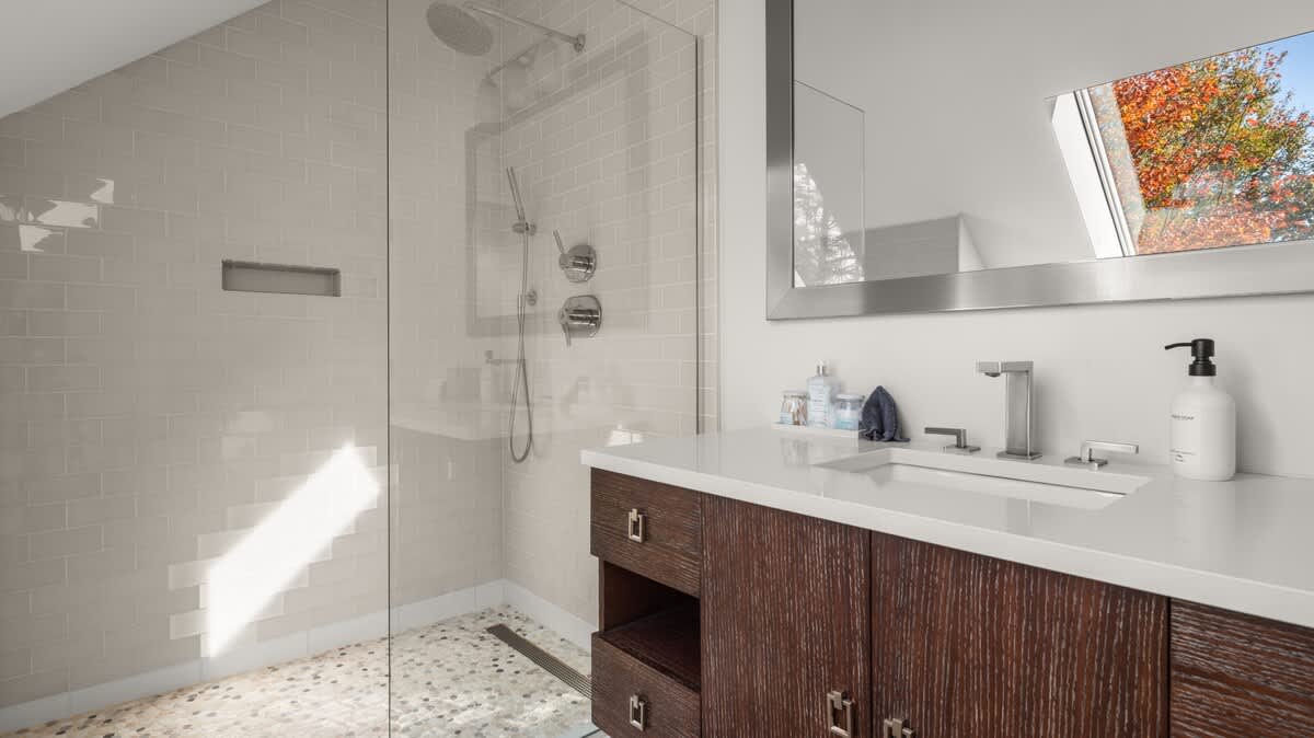 Modern bathroom with a spacious walk-in shower featuring light subway tiles and a glass enclosure, a dark wood vanity with a white countertop, and a large mirror.