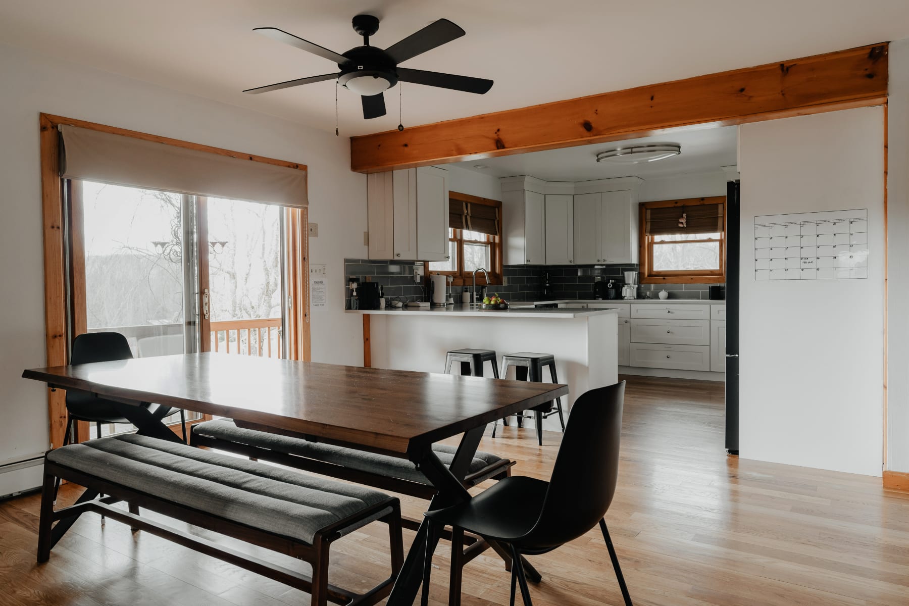 A spacious dining area featuring a long wooden table with benches and chairs, set against a backdrop of a modern kitchen with white cabinetry and a large island. Hardwood floors extend throughout the open-concept space.