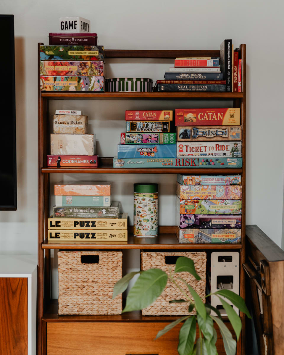 A tall wooden bookshelf neatly organized with a diverse collection of board games and puzzles, indicating a dedicated space for entertainment and family fun. Woven baskets are stored on the bottom shelf.