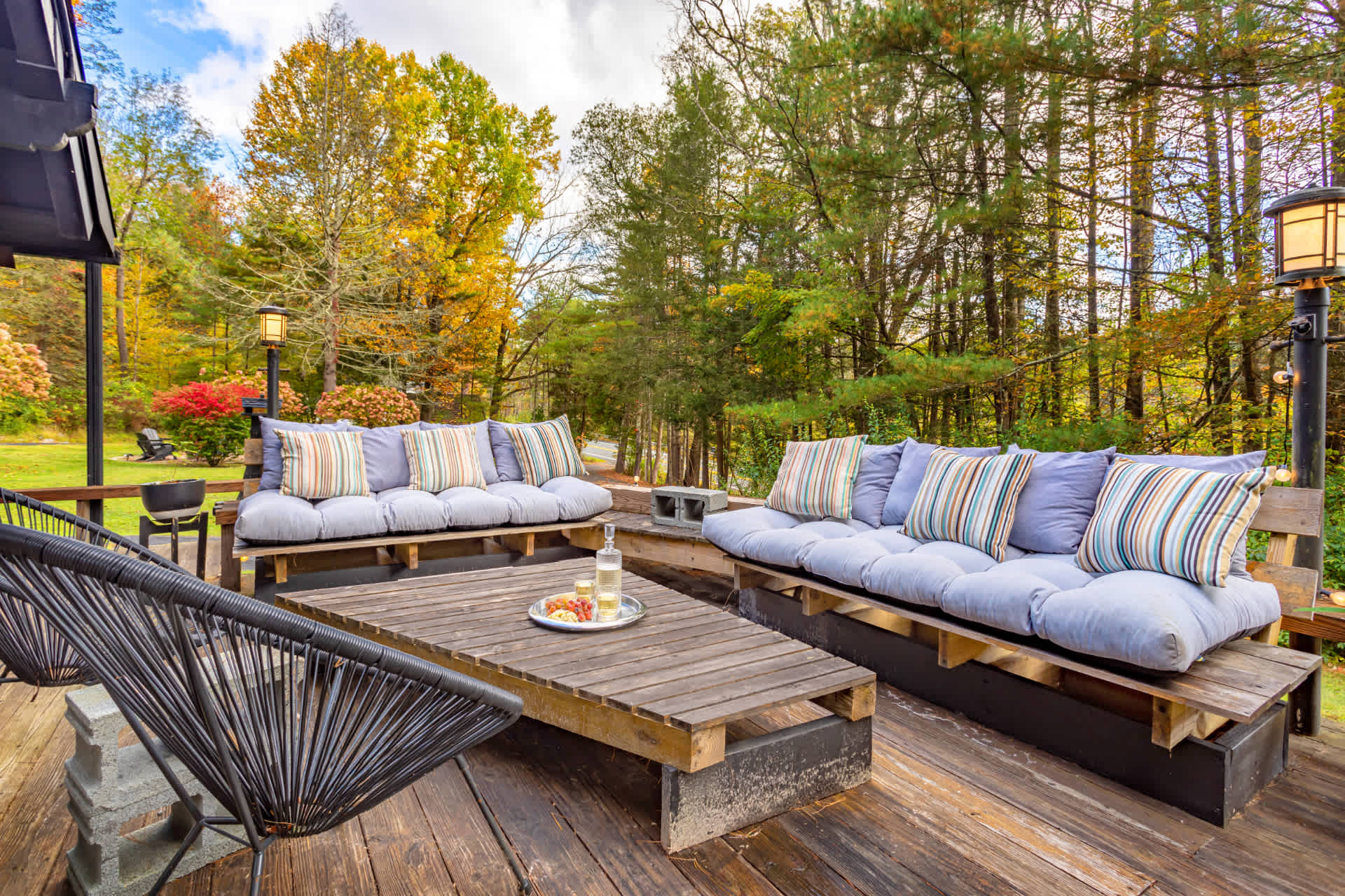 Spacious wooden deck with two large built-in sofas featuring light blue cushions and striped pillows, a wooden coffee table, and surrounded by lush trees.