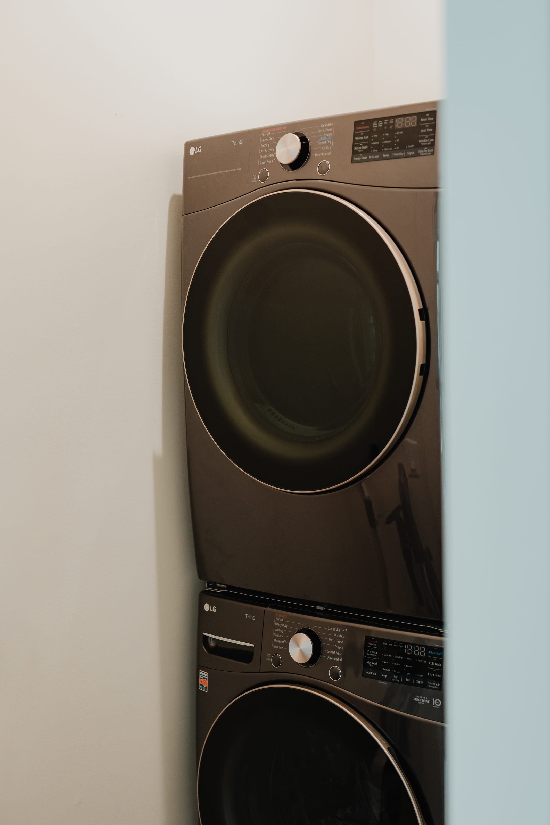 Stacked dark grey LG washer and dryer unit with digital displays and control knobs, set against a white wall in a dedicated laundry area.