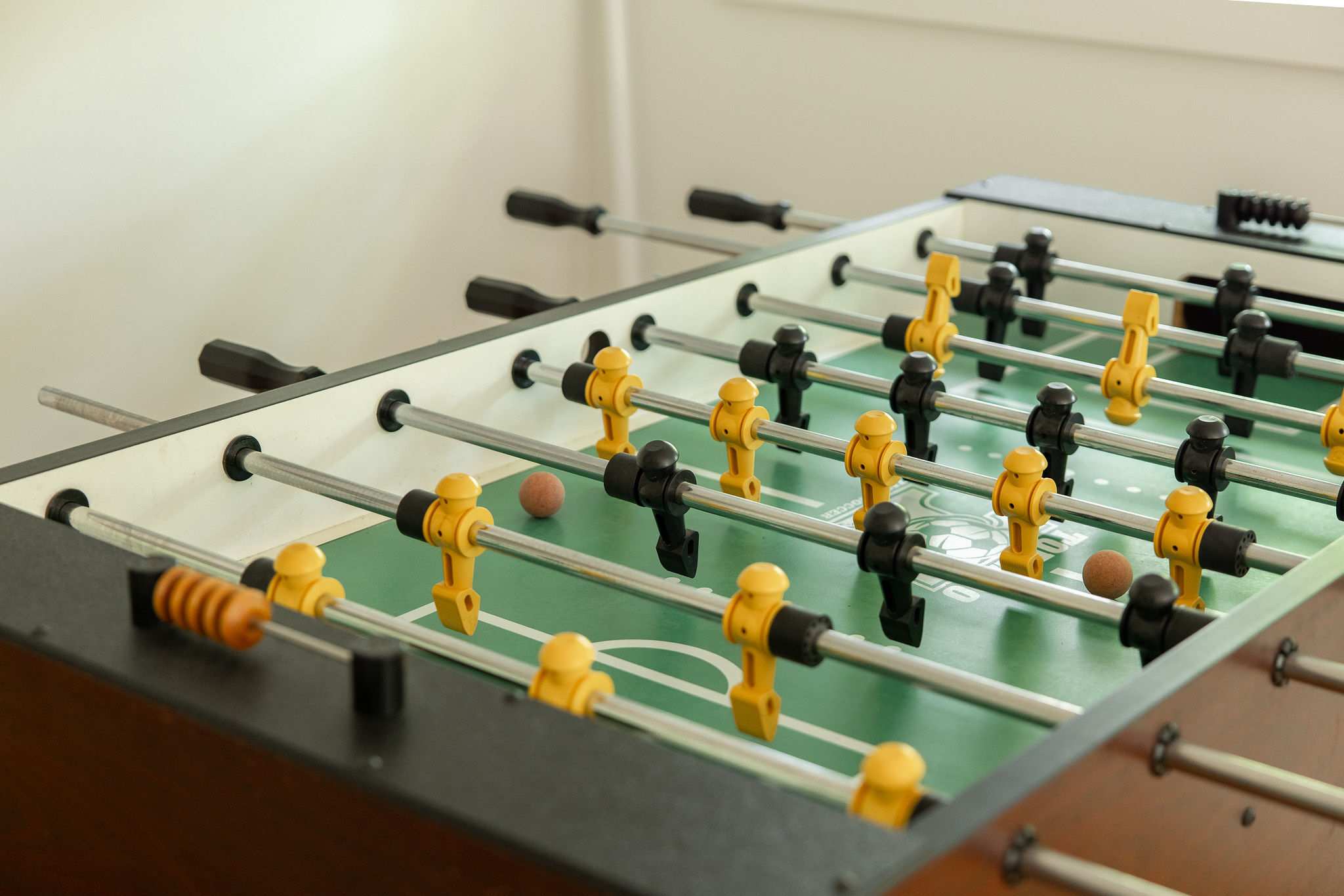 Close-up view of a classic foosball table with yellow and black players, set against a light-colored wall, suggesting a dedicated game area.