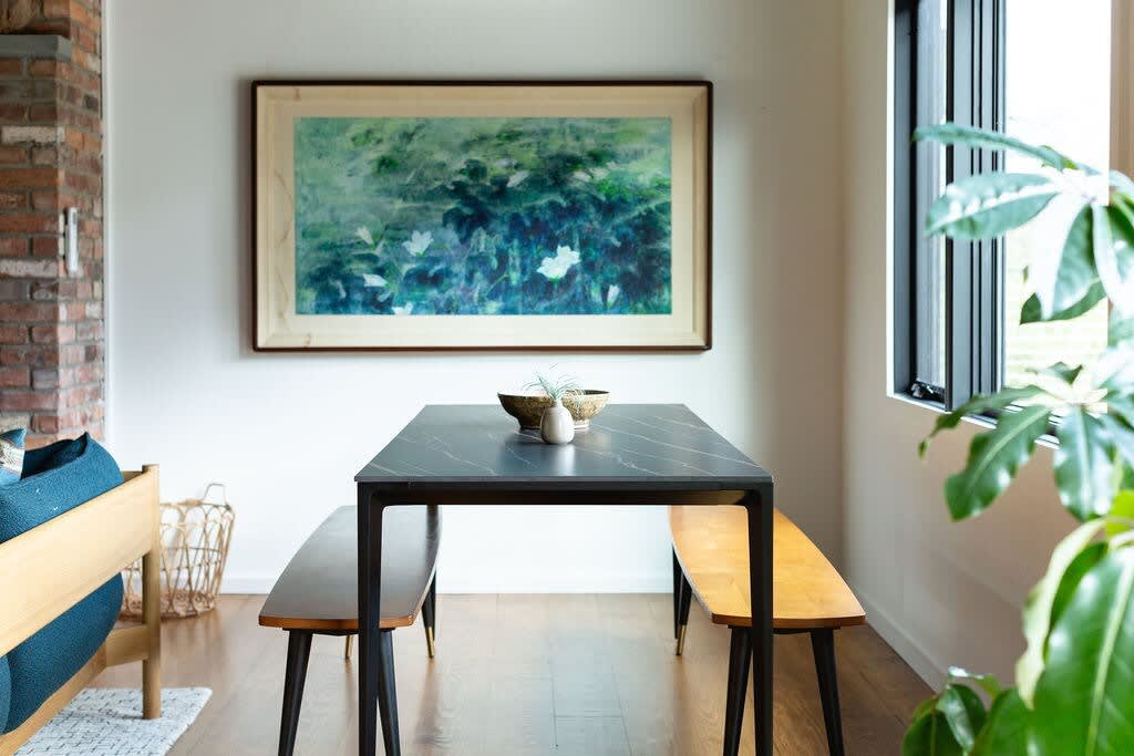 Modern dining area featuring a black rectangular table, two wooden benches, and a large abstract painting with green and blue hues hanging on a white wall.