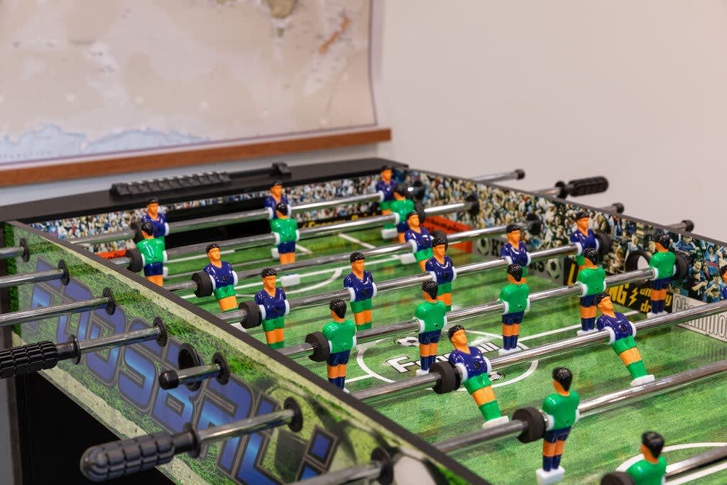 Close-up of a foosball table with blue and green player figures, set against a blurred background, indicating a dedicated game area.