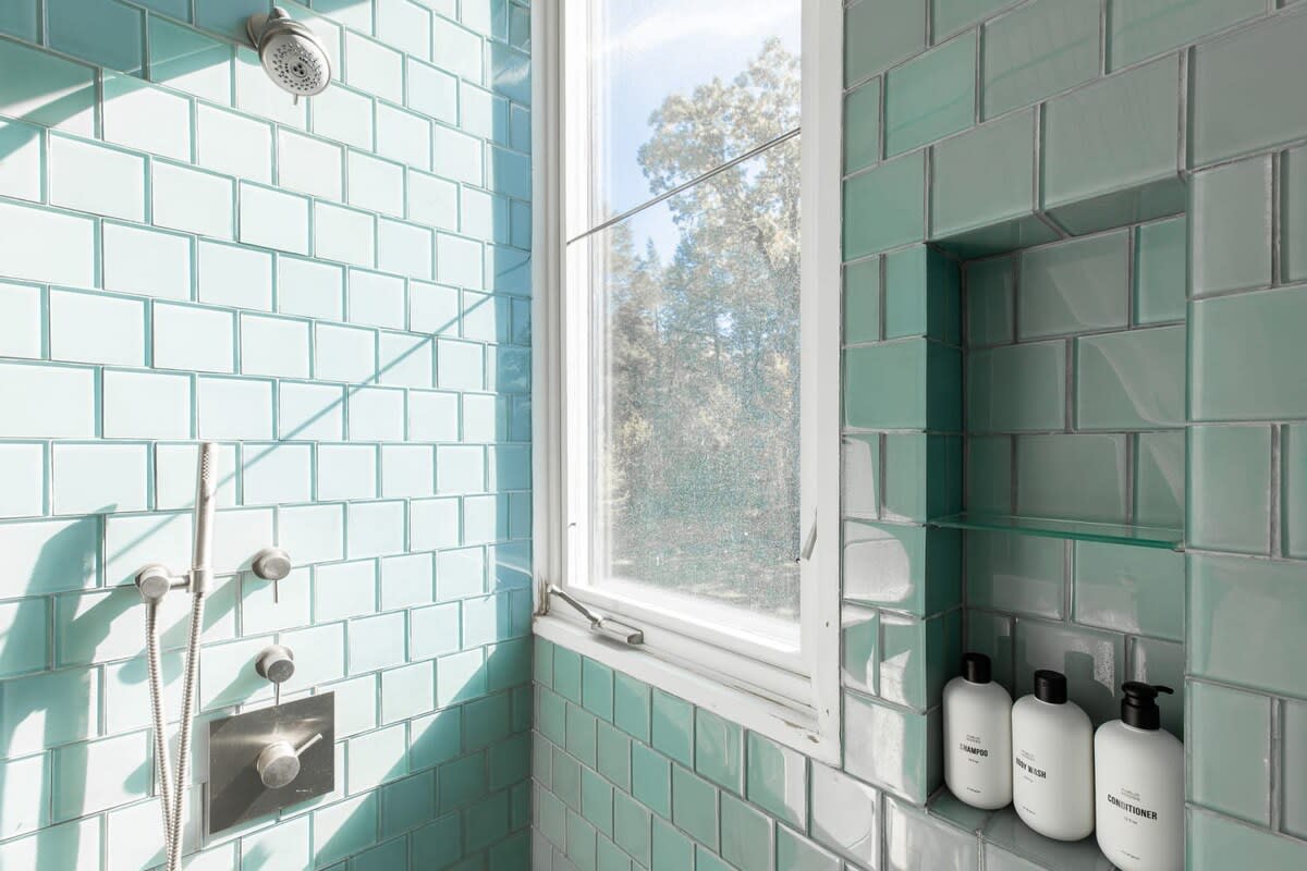 A bright shower area featuring light blue subway tiles, a window providing natural light, and a built-in niche with glass shelves for toiletries.