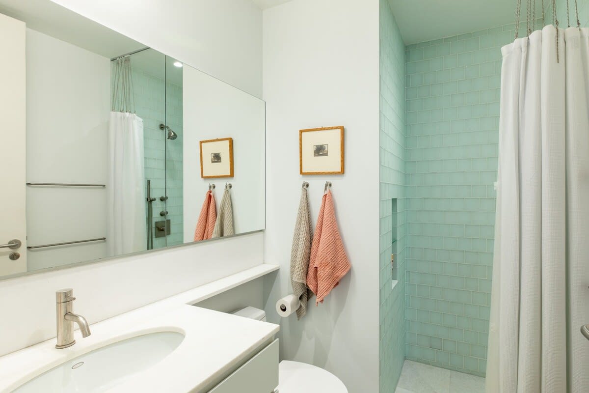 Modern bathroom with a white vanity and sink, a large mirror, and a shower featuring light blue square tiles and a white shower curtain, providing a clean and refreshing aesthetic.
