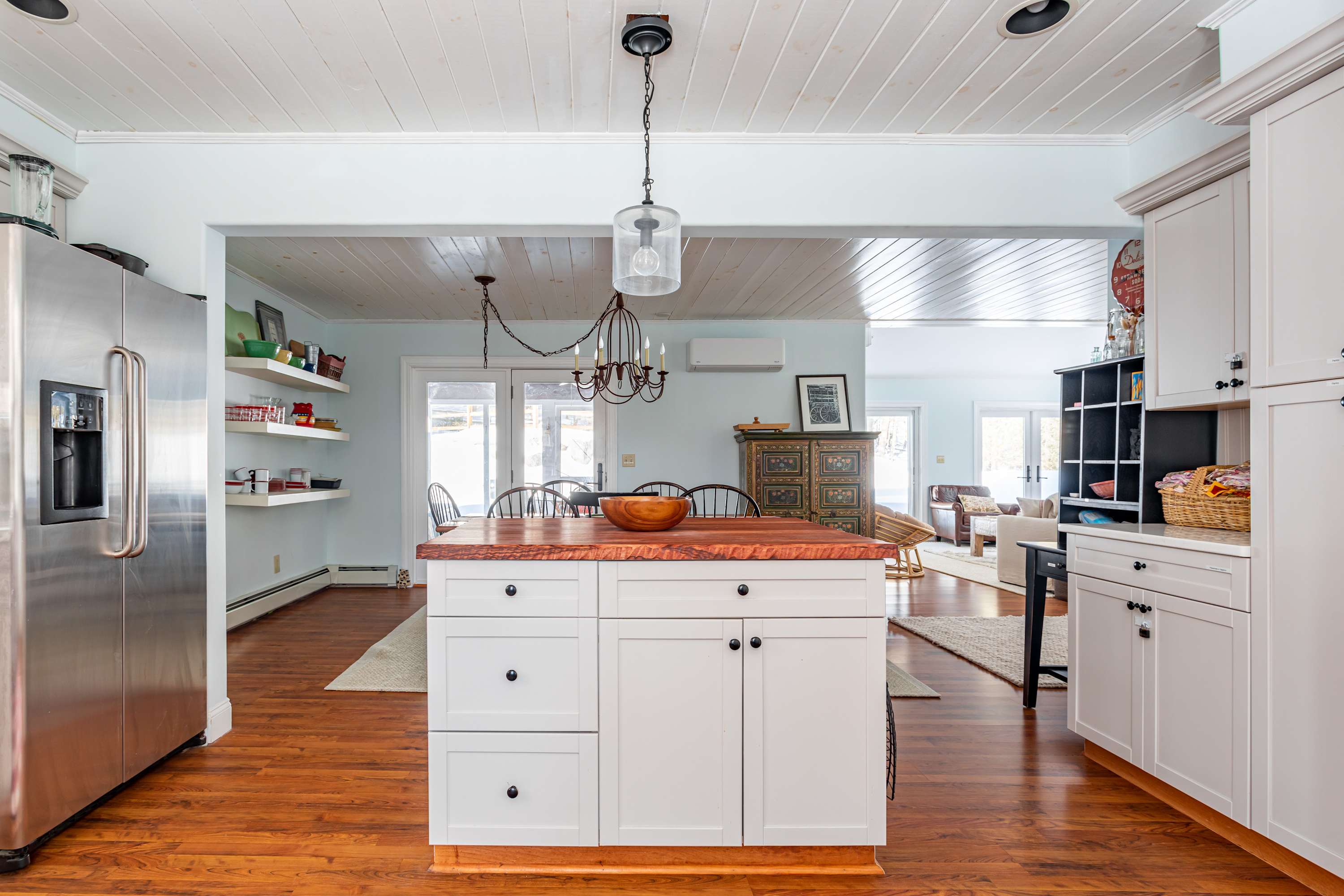 A view of the kitchen island with a wooden butcher block countertop and white cabinets, looking towards the dining area and living room, showcasing the open-concept layout.