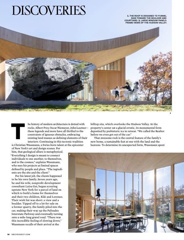 A magazine spread showcasing the interior and exterior of the unique house, featuring a massive natural rock integrated into the design and a deck with outdoor seating overlooking the forest.