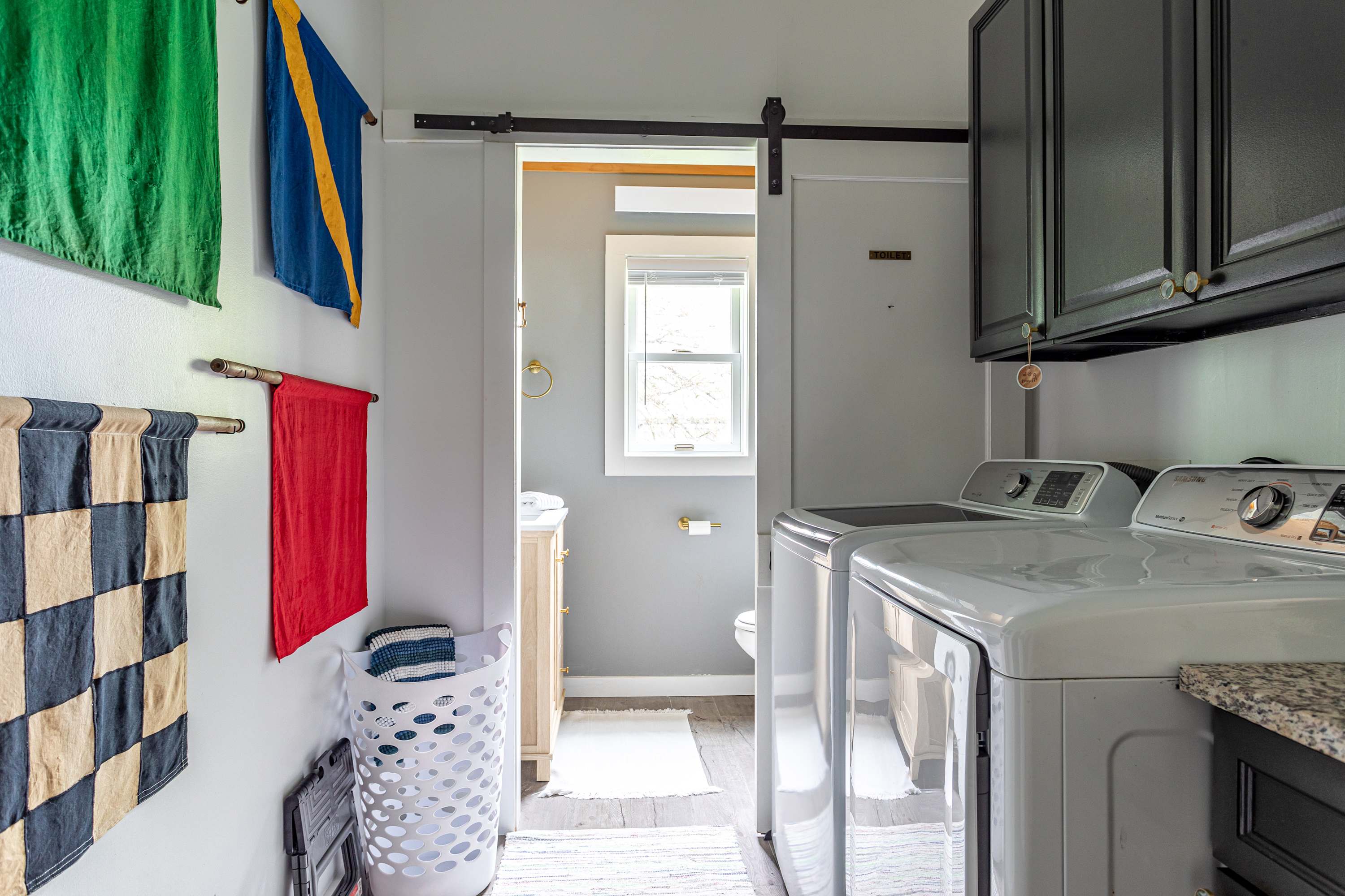 Functional laundry room equipped with a white washer and dryer, black upper cabinets, and a granite countertop. A sliding barn door reveals a partial view of an adjacent bathroom.