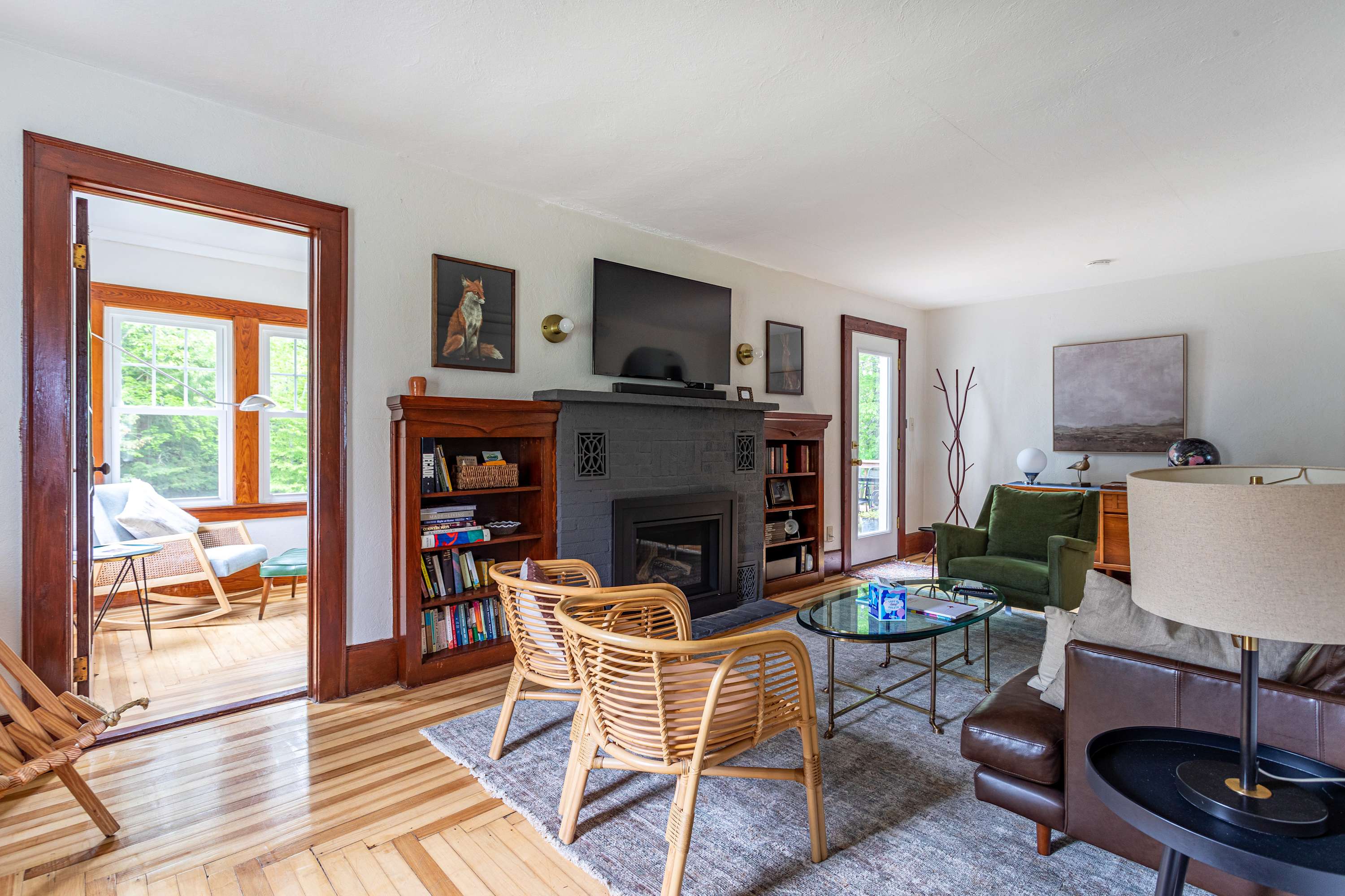 A comfortable living room with a brown leather sofa, a dark gray fireplace flanked by built-in bookshelves, and a glass coffee table, leading to another room through a wide doorway.