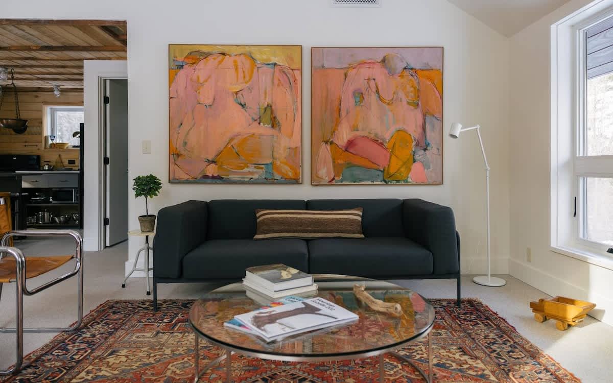 A modern living room features a dark gray sofa with a striped pillow, a glass coffee table, and two large abstract paintings on the wall, all set on a patterned area rug.