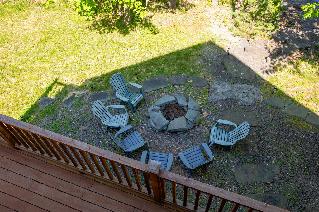 Overhead view of an outdoor fire pit made of stacked stones, surrounded by six light blue Adirondack-style chairs on a gravel and grass patch.