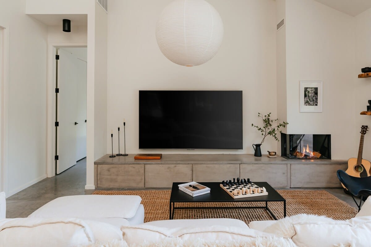 A bright living room with a high vaulted ceiling and a large white paper lantern, centered around a wall-mounted TV above a concrete console, a modern fireplace, and a comfortable white sectional sofa.