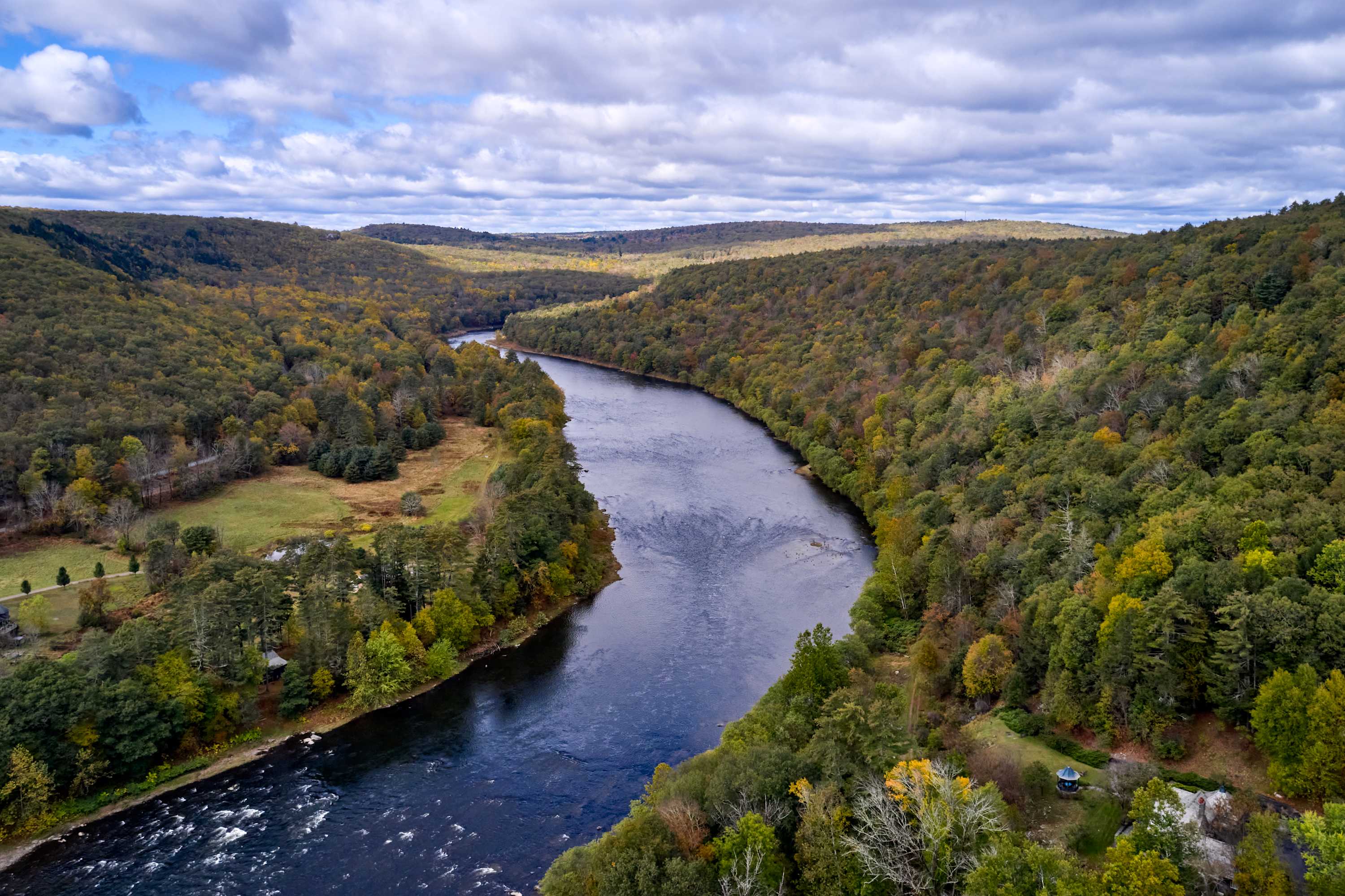 An expansive aerial view showcases a wide, winding river cutting through vast, tree-covered mountains displaying early autumn colors under a partly cloudy sky, highlighting the property's secluded natural setting.