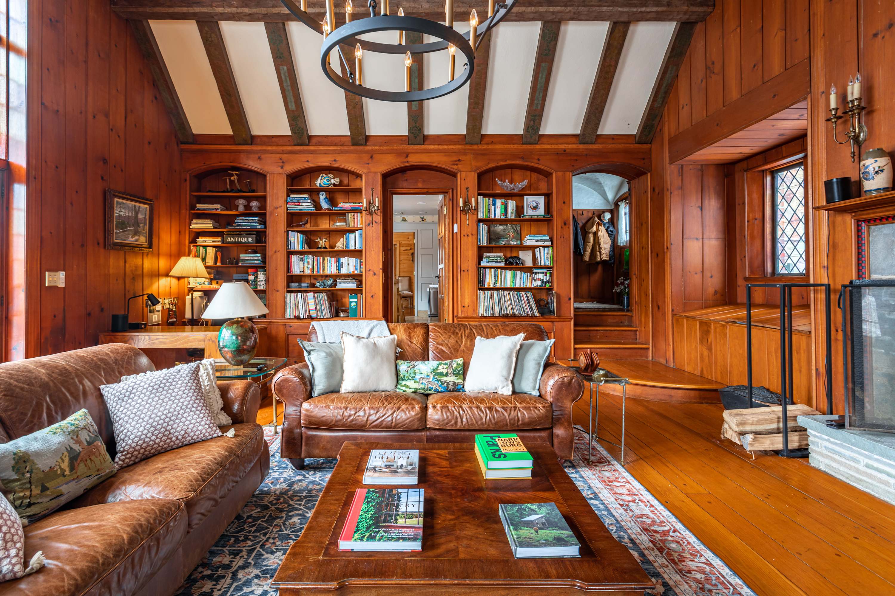 A view of the living room highlighting the built-in bookshelves flanking an arched doorway, filled with various books and decorative items. A brown leather sofa with throw pillows and a wooden coffee table are central on a patterned rug.