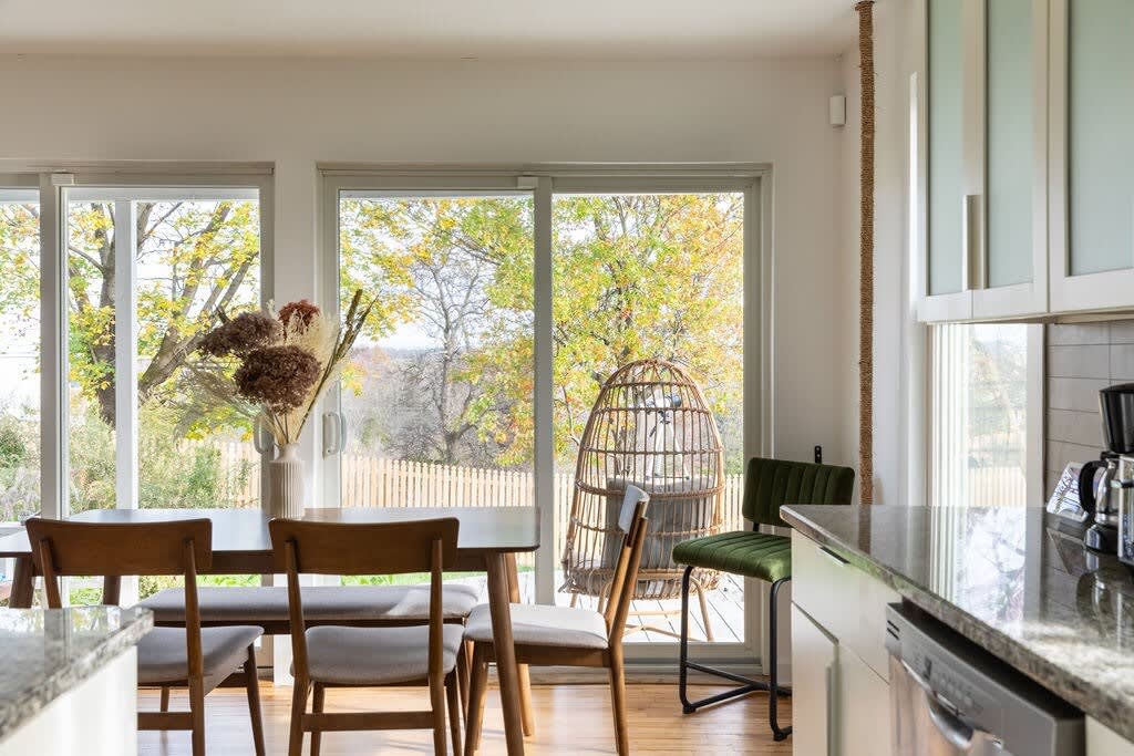 Dining area adjacent to the kitchen, featuring a wooden dining table with chairs and large sliding glass doors offering views of the backyard. A unique rattan egg chair adds a decorative touch.