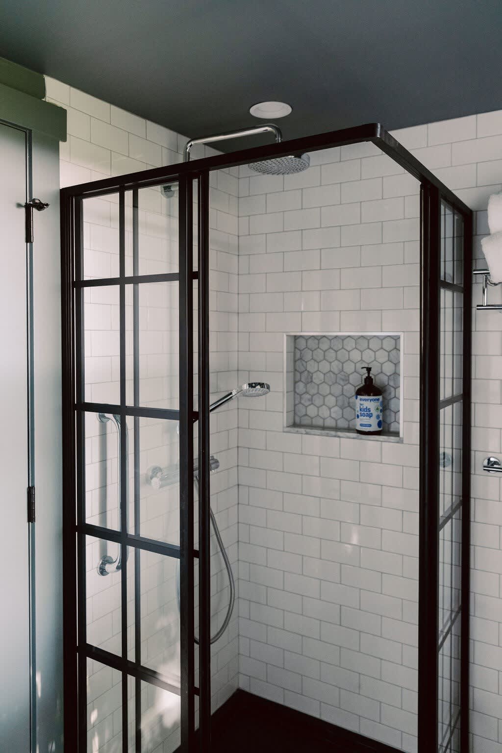 Modern walk-in shower with a black-framed glass enclosure, white subway tile walls, a built-in hexagonal tile niche, and a rain shower head, providing a sleek and functional bathing space.