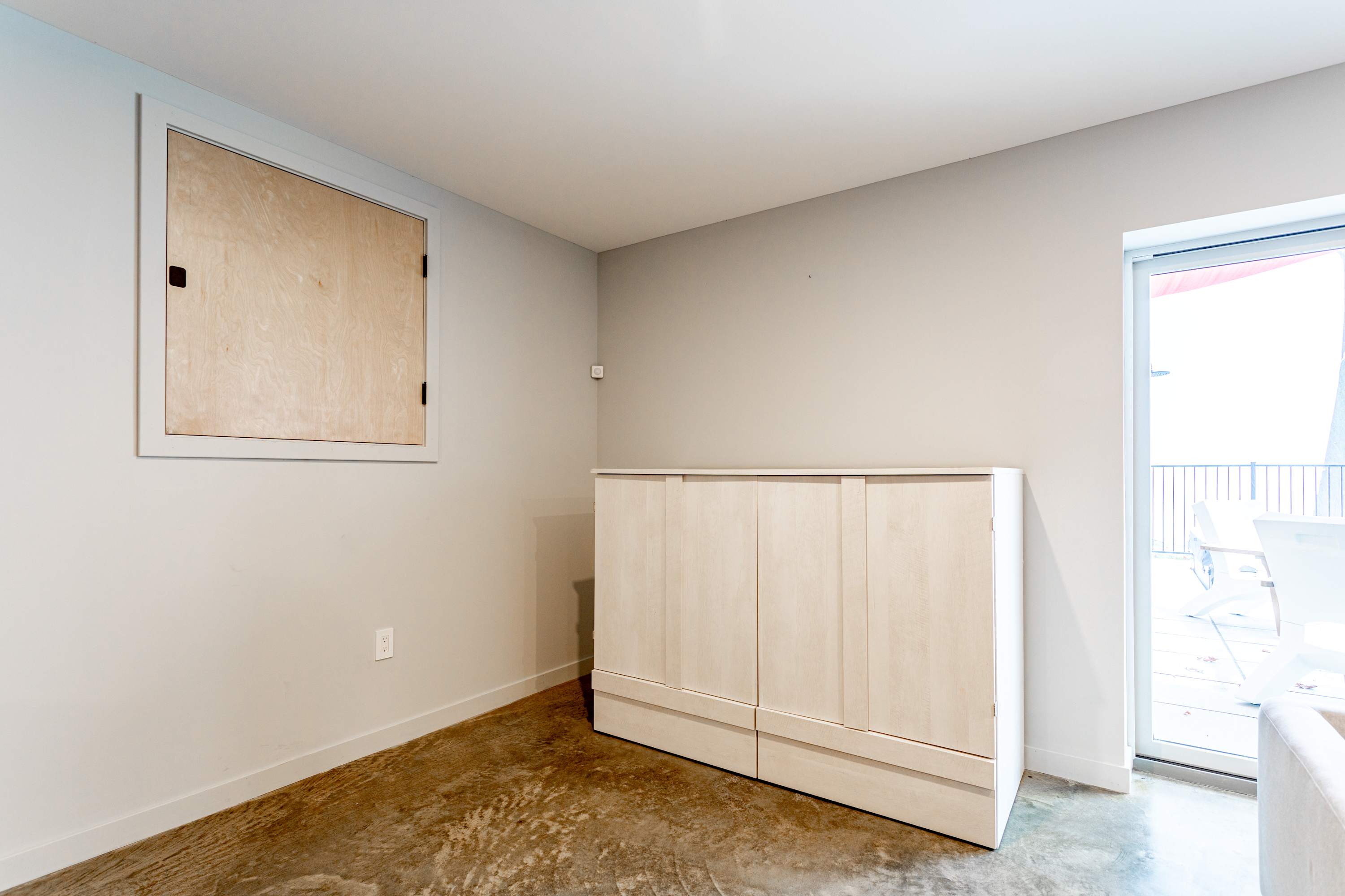A view of the secondary living space showing the closed murphy bed cabinet, a light wooden panel on the wall, and a sliding glass door providing access to an outdoor area, highlighting the versatile use of the space.