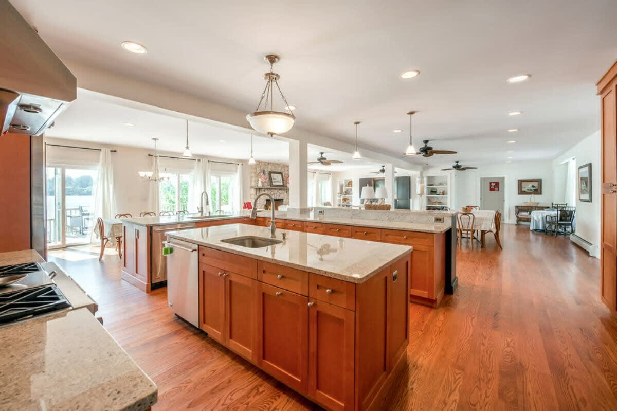 Open-concept kitchen with multiple light wood islands and granite countertops, connecting to the living and dining areas, featuring hardwood floors and recessed lighting.