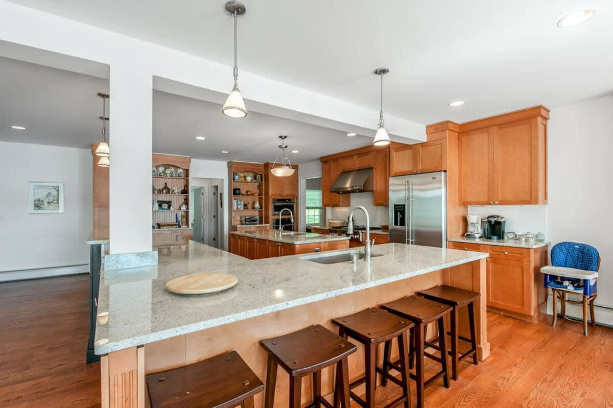 A spacious open-concept kitchen boasts light wood cabinetry, stainless steel appliances, and two large islands with granite countertops and bar seating. Pendant lights illuminate the functional and inviting space with hardwood floors.