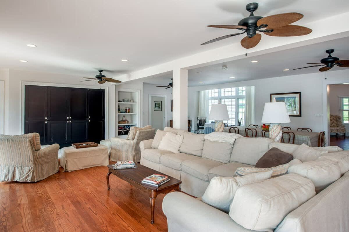 Spacious living area featuring a large light-colored sectional sofa, dark built-in cabinets, and hardwood floors, with a ceiling fan and recessed lighting.