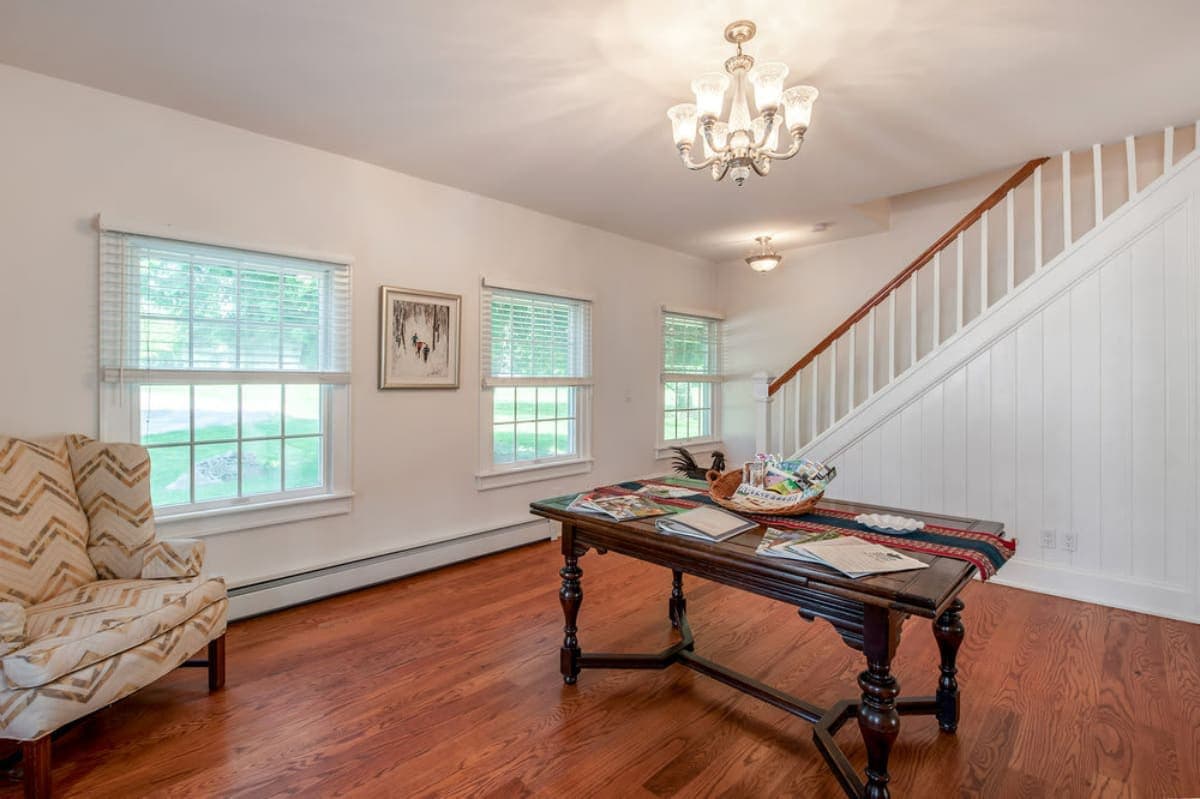 Inviting foyer area with warm hardwood floors, a traditional wooden console table, and a white staircase with a wooden handrail, illuminated by natural light from multiple windows.