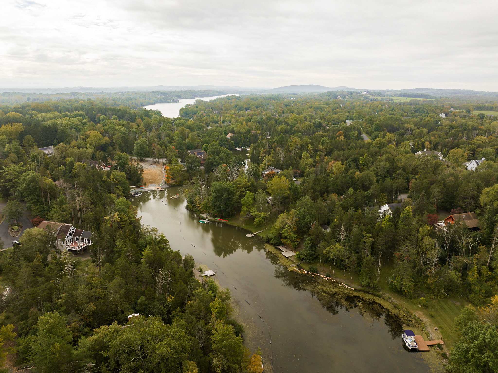 Aerial view of a winding lake surrounded by dense green forests and scattered houses, under a cloudy sky, showcasing the property's waterfront location.