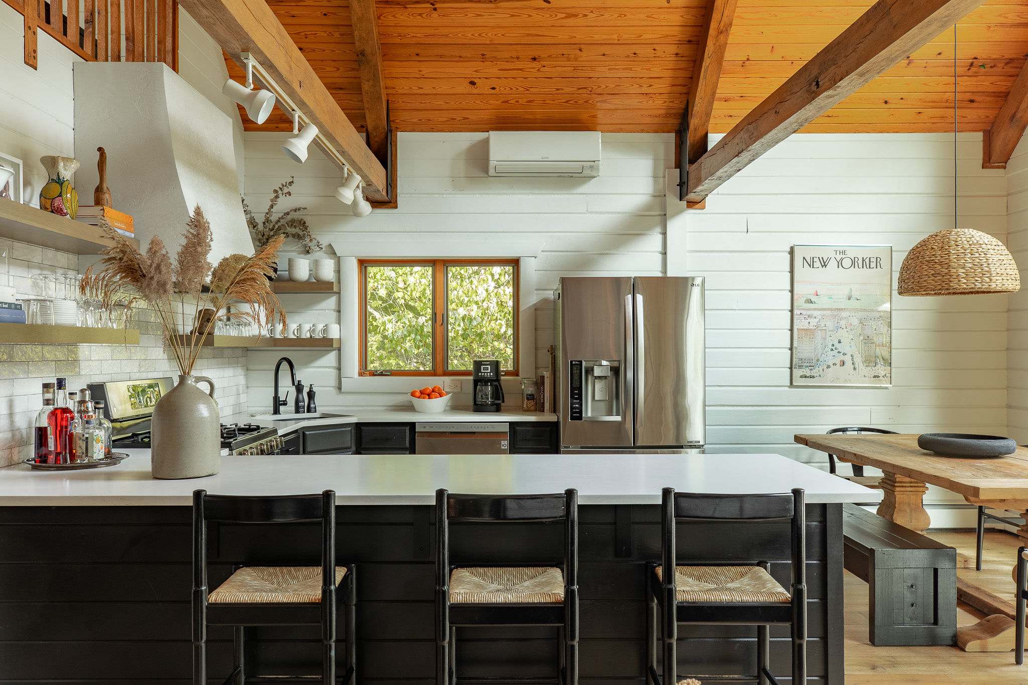 Well-lit kitchen with a large island featuring bar seating, black cabinets, white countertops, and stainless steel appliances, complemented by a wooden ceiling and shiplap walls.