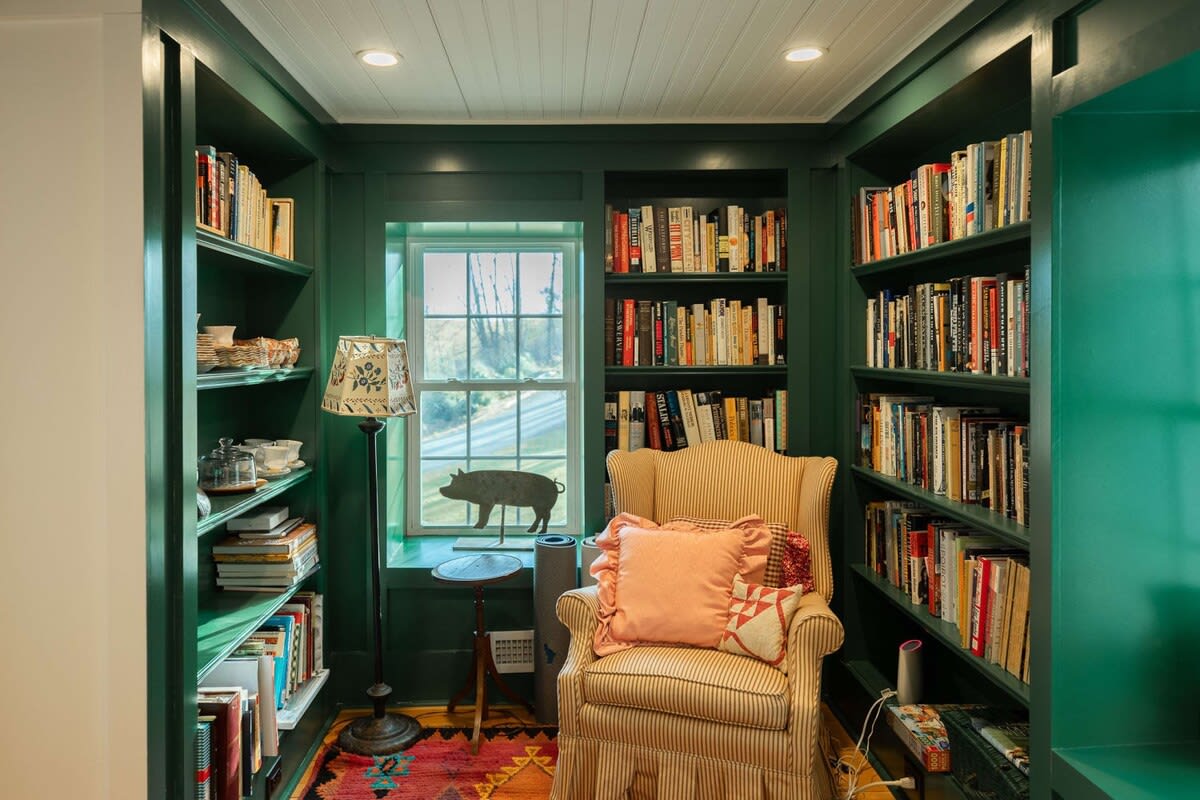 A vibrant green library/office space features built-in bookshelves filled with books, a cozy striped armchair, and a colorful patterned rug. A window provides natural light, with a decorative pig silhouette on the sill.