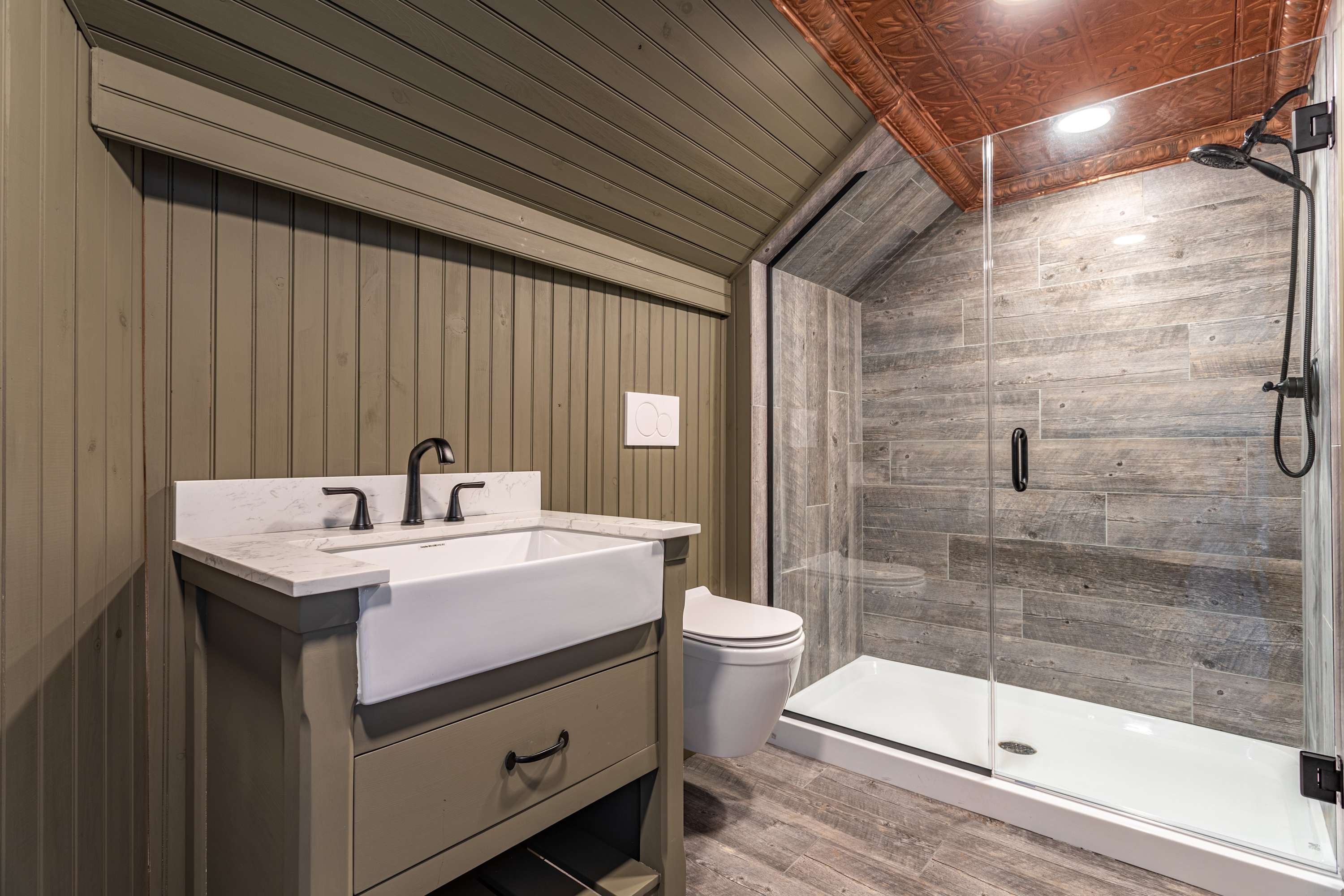 Modern bathroom featuring a walk-in shower with wood-look tile, a white farmhouse sink vanity with a marble top, and light green wood paneling on the walls and ceiling.