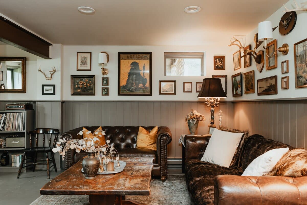 A detailed view of the game room's seating area, showcasing two brown leather sofas, a rustic wooden coffee table, and a gallery wall filled with vintage art and taxidermy, creating a warm, inviting atmosphere.
