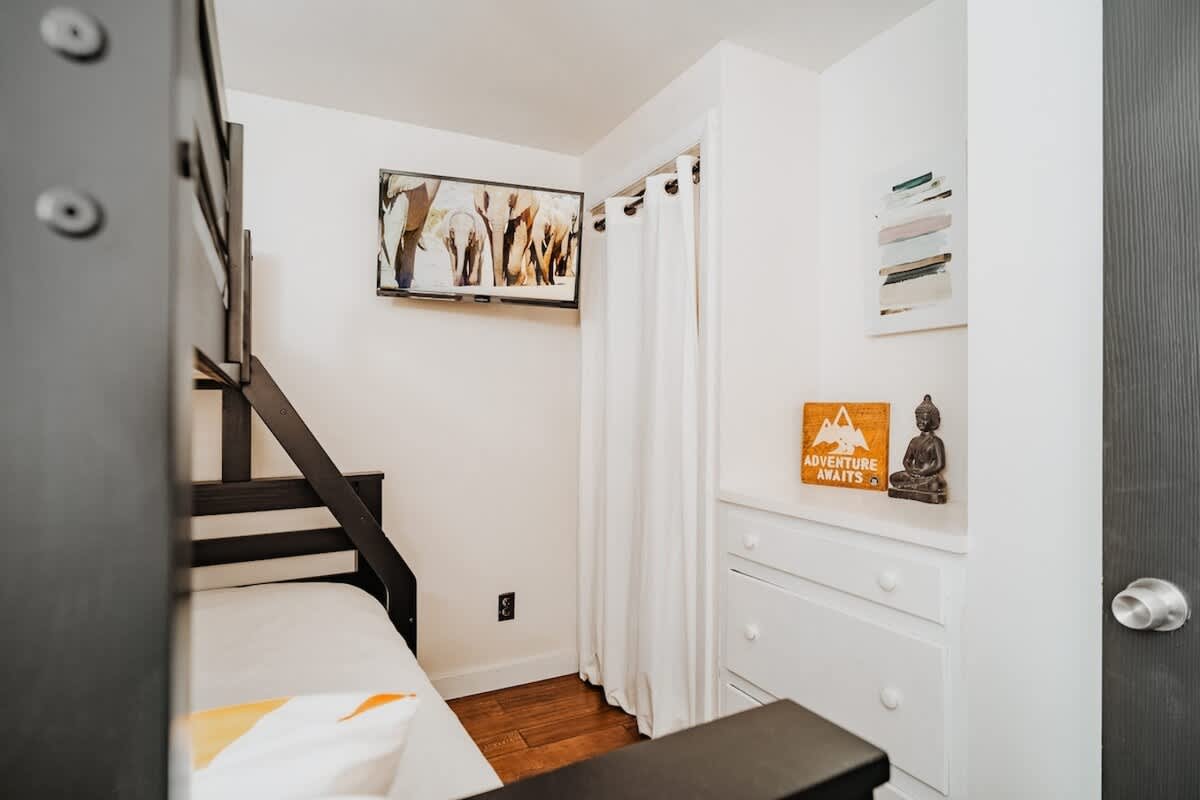Functional bunk bed room featuring a wall-mounted TV, a white dresser with a curtained storage area, and a small Buddha statue, optimizing space for comfort and entertainment.