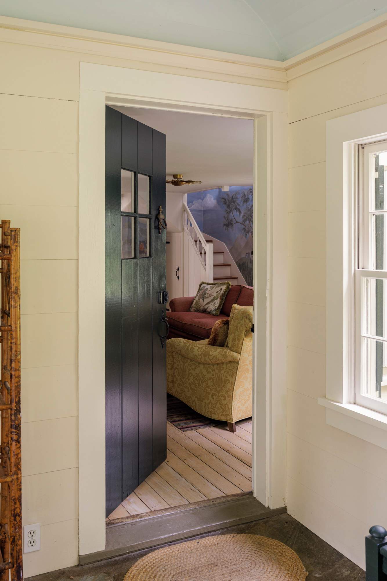 A dark blue paneled door with small windows opens into a cozy interior with light wood floors and a glimpse of a living area beyond. The walls are painted a soft cream, and a small round rug sits on the floor.