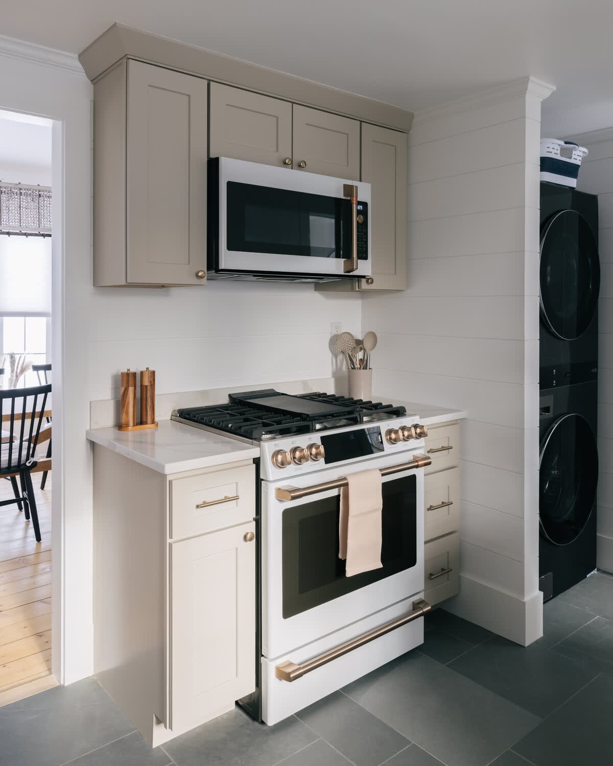 A kitchen section featuring a white and brass range with a griddle, an over-the-range microwave, and light gray cabinets, with stacked black washer and dryer units visible in the adjacent laundry area.