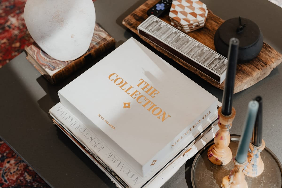 A detailed shot of the coffee table in the living room, displaying a stack of books, decorative candles, and a white vase. Various small decorative items are arranged on a wooden tray, adding a touch of curated style.