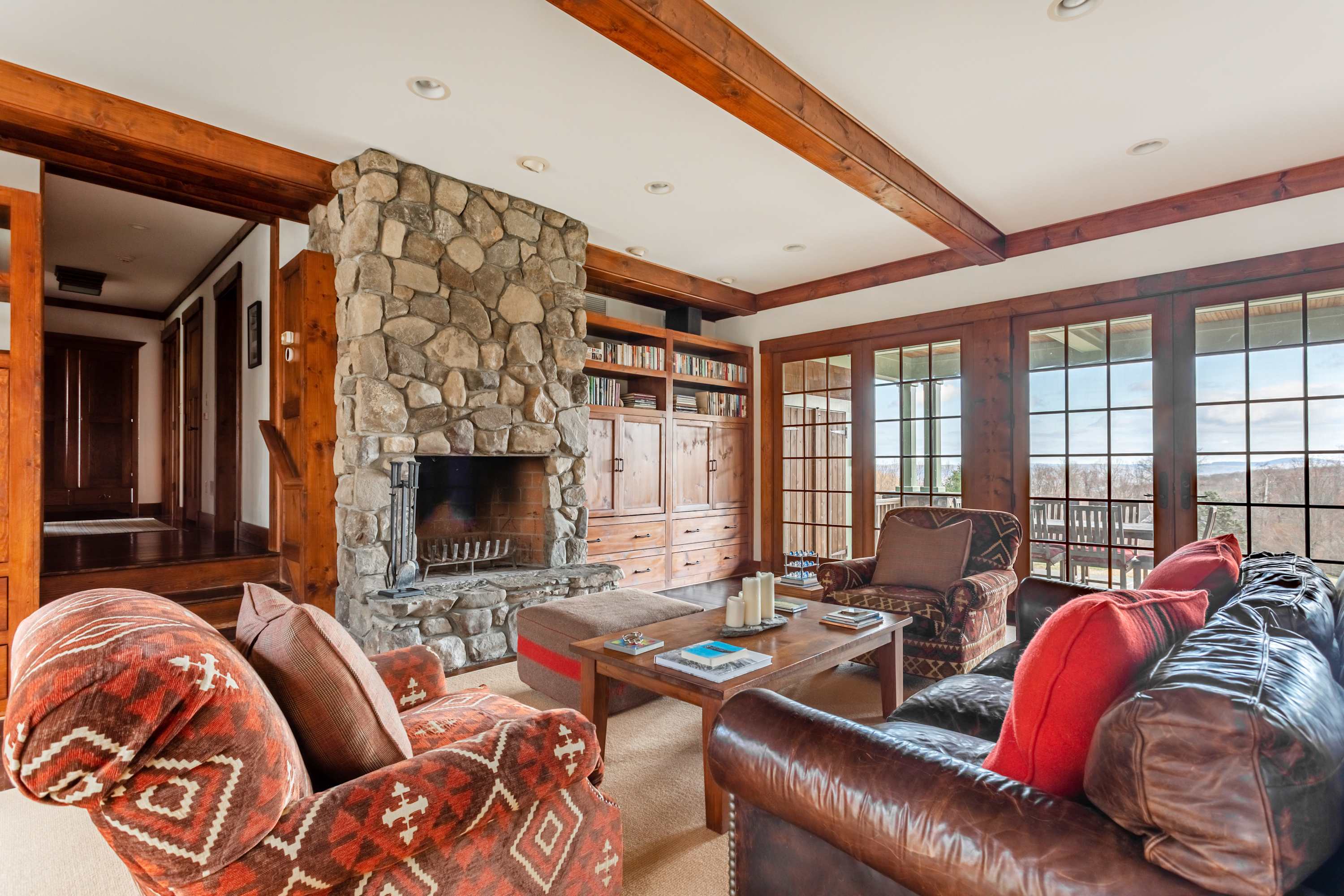 Inviting living room centered around a massive stone fireplace with built-in wooden shelving. Comfortable sofas and armchairs are arranged around a coffee table, with large windows offering panoramic mountain views.