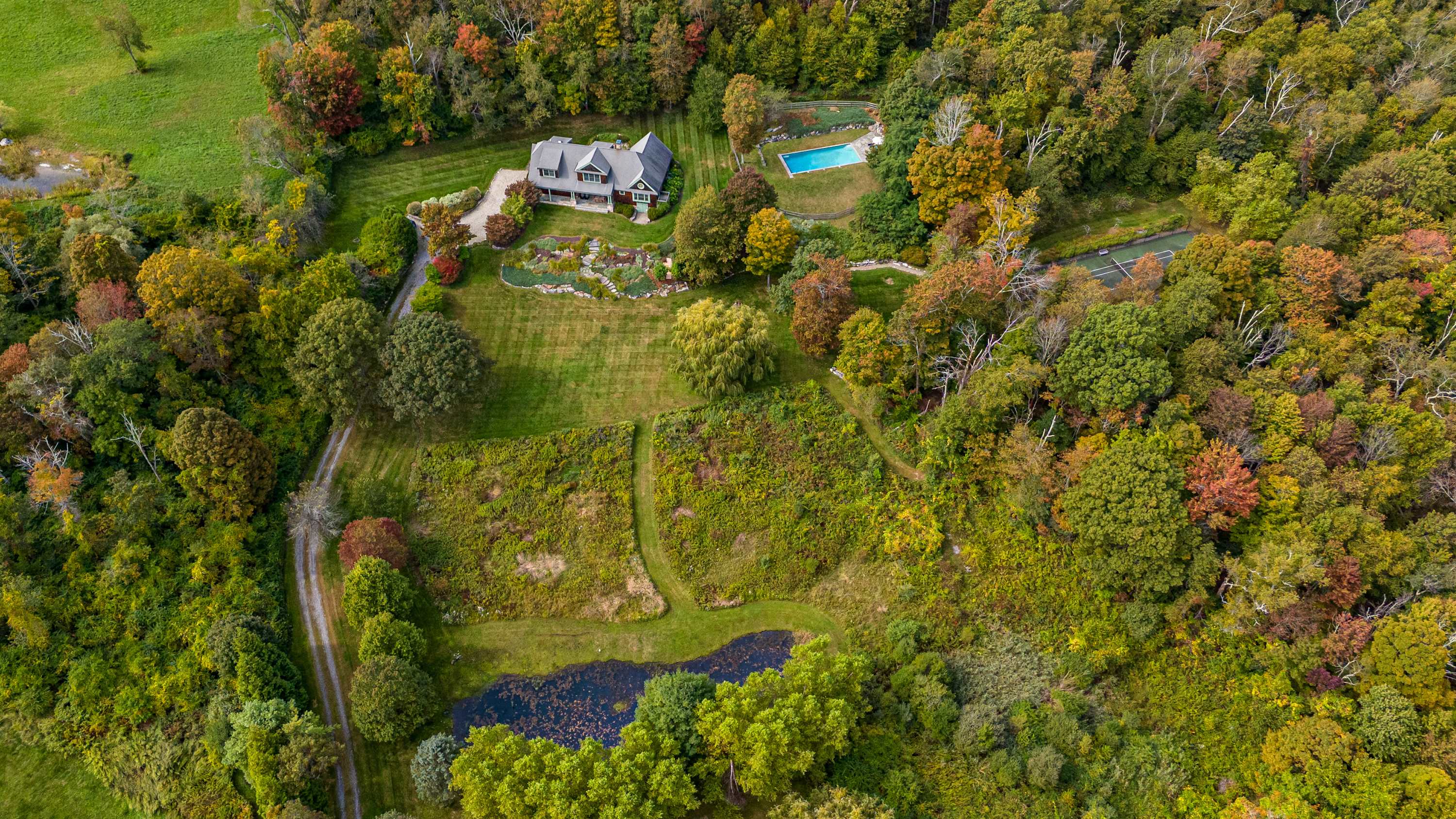 An expansive aerial shot captures the entire property, including the house, swimming pool, and a natural pond, all integrated into a vast, undulating landscape of dense forest and open fields with vibrant autumn colors.