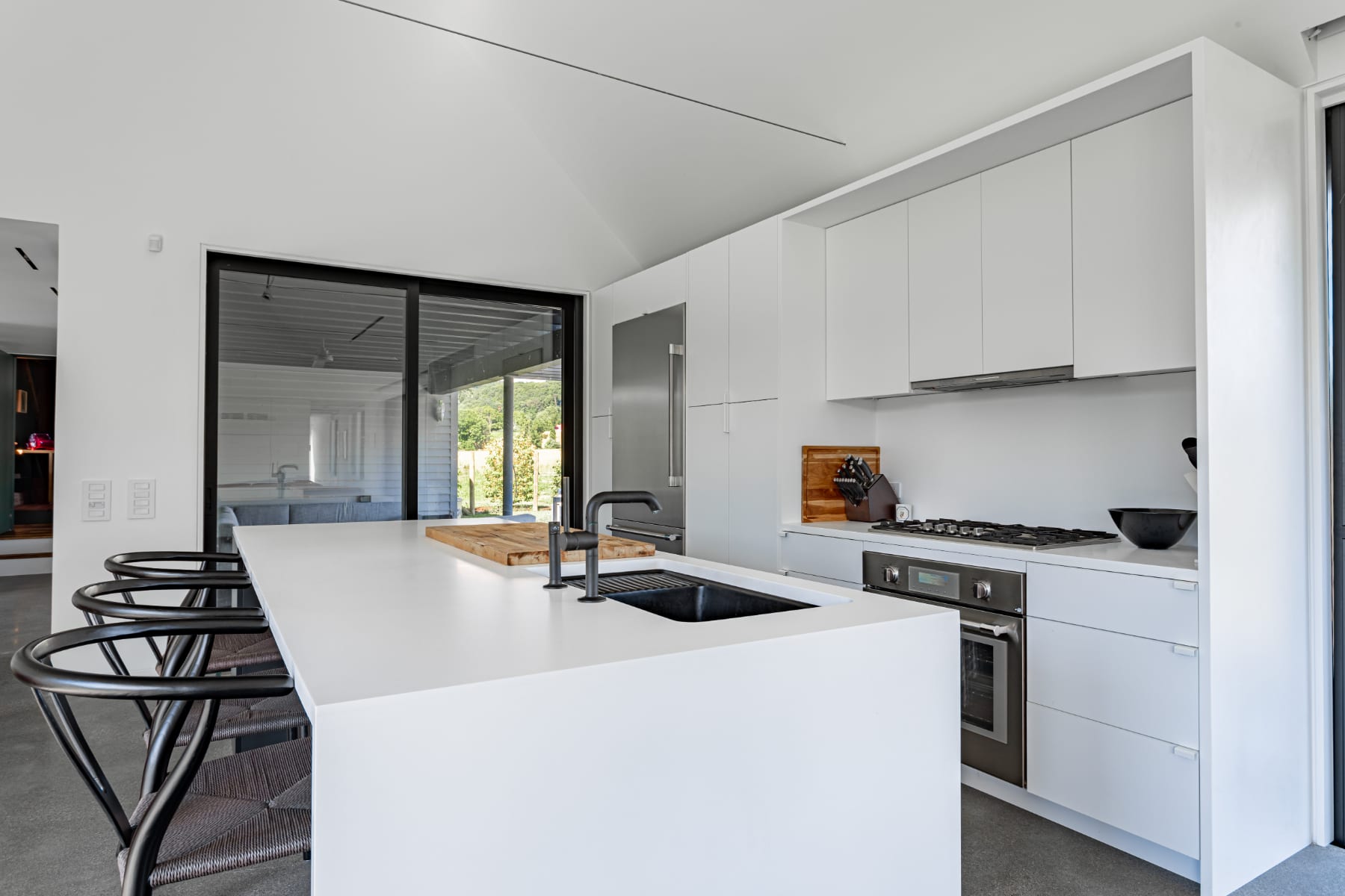 Sleek, modern kitchen featuring white flat-panel cabinetry, a large white island with an integrated black sink, stainless steel refrigerator, and a gas range, all set on polished concrete floors.