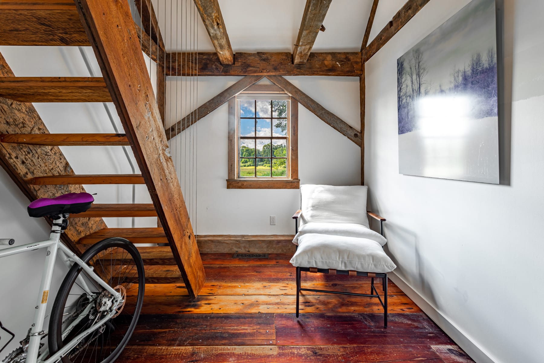 Rustic landing area featuring a wooden staircase with cable railings, exposed wooden beams, and rich hardwood floors, with a small window offering a glimpse of the outdoors.