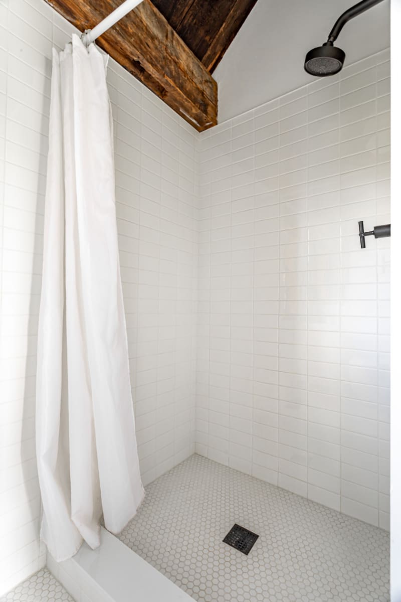 Modern shower stall with white subway tile walls, a white hexagonal tile floor, and a black rain shower head, featuring a white shower curtain.