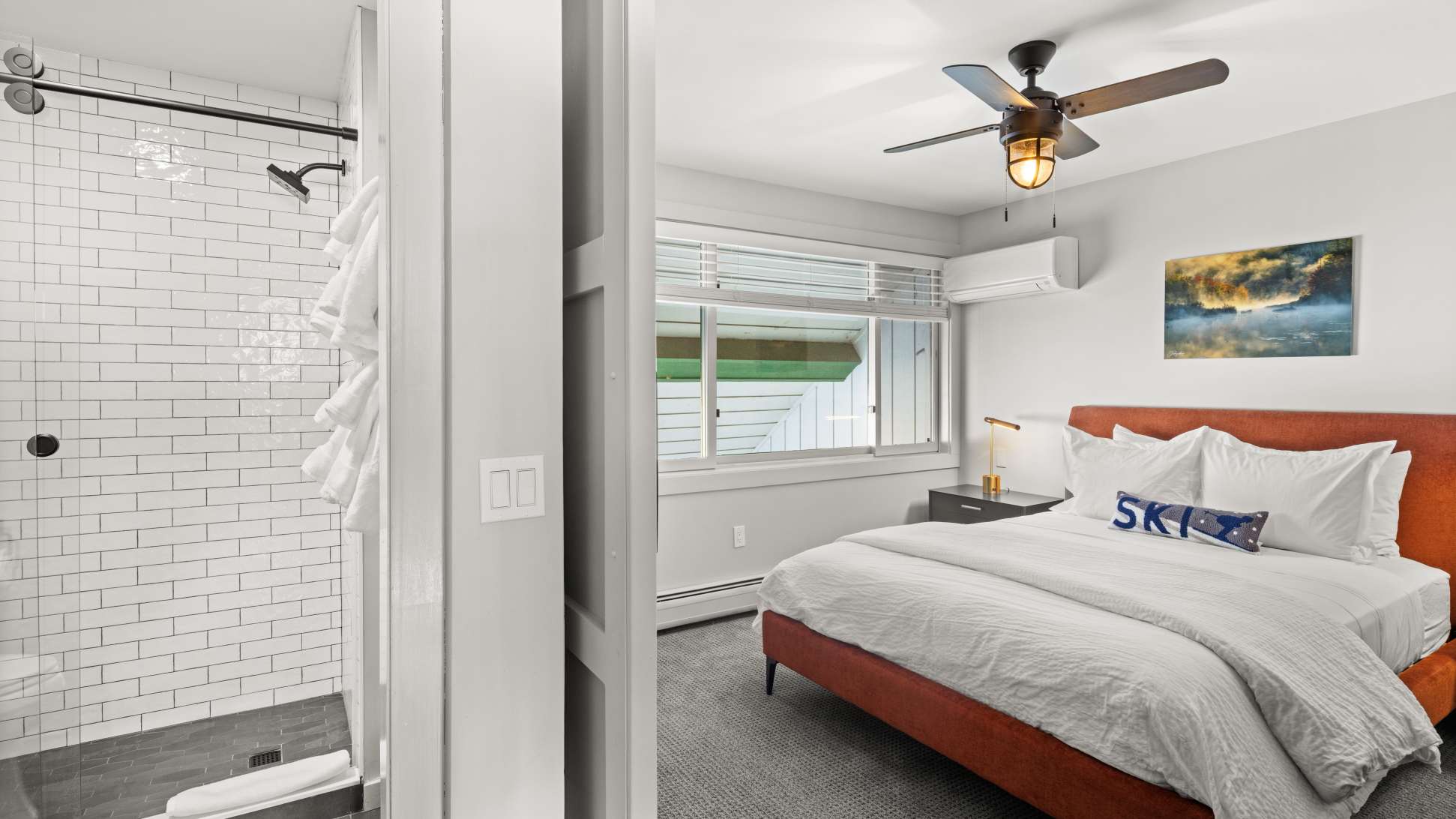 View of bedroom-1 with an orange bed and white bedding, showing an open doorway leading to a bathroom with a white subway tile shower.