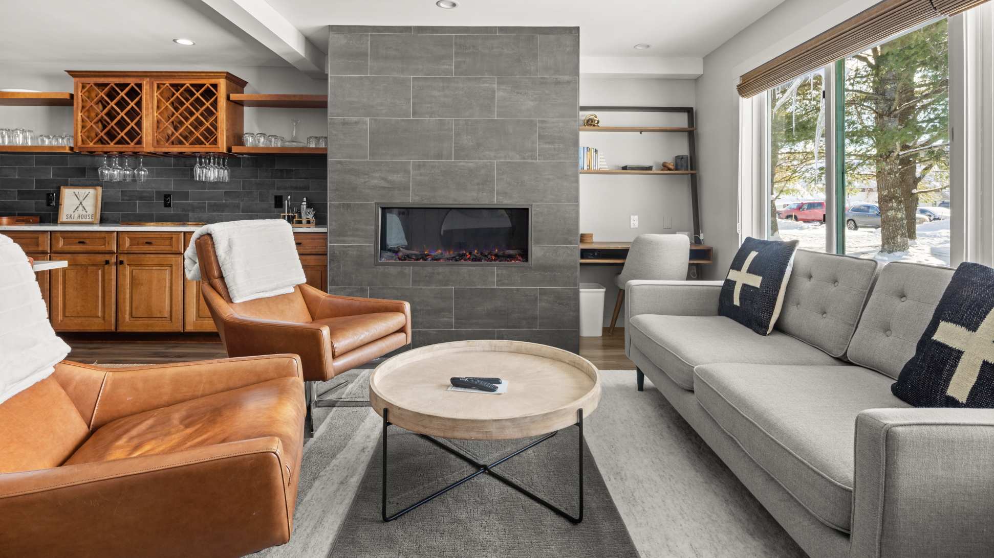 Inviting living room featuring a gray sofa with decorative pillows, two brown leather armchairs, and a round wooden coffee table. A sleek, modern fireplace with gray tile extends to the ceiling.