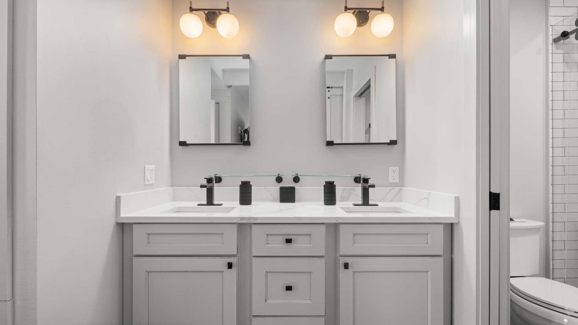 Modern bathroom featuring a double vanity with white marble countertops, two rectangular mirrors, and sleek black faucets and light fixtures.