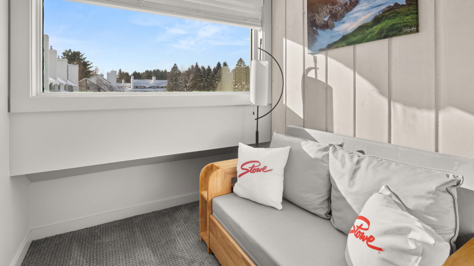 Bright nook with a light wood daybed or sofa, gray cushions, and 'Stowe' branded pillows. A large window offers a scenic view of a snowy outdoor landscape.