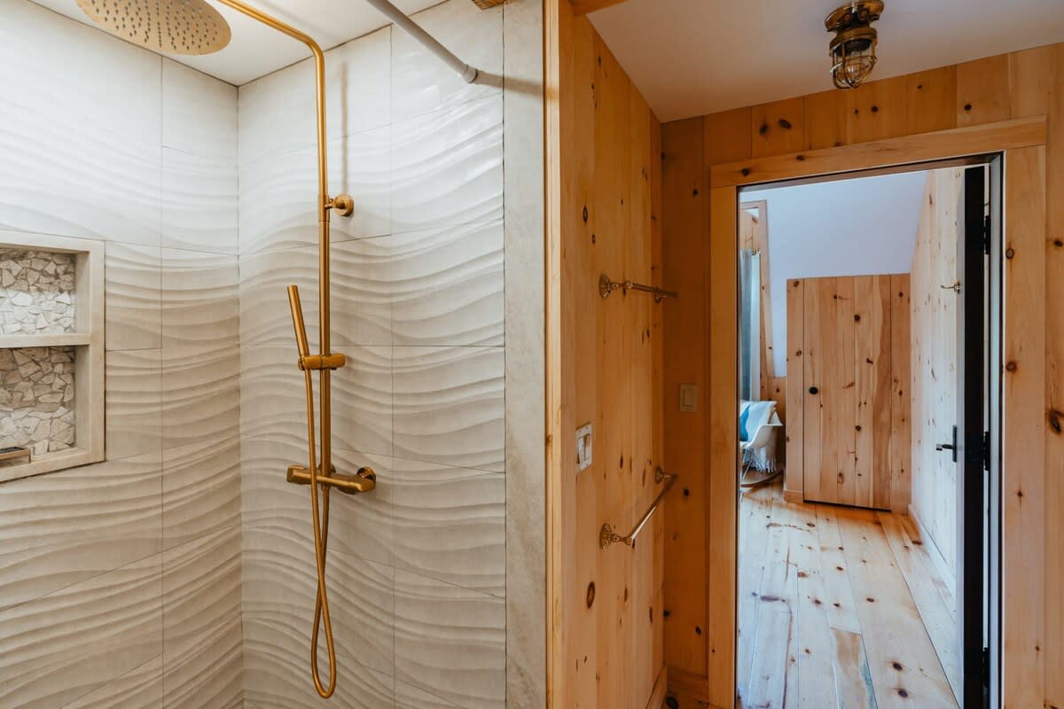 Modern shower with textured white wavy tiles, a built-in niche for toiletries, and elegant gold-toned shower fixtures, offering a luxurious bathing experience.