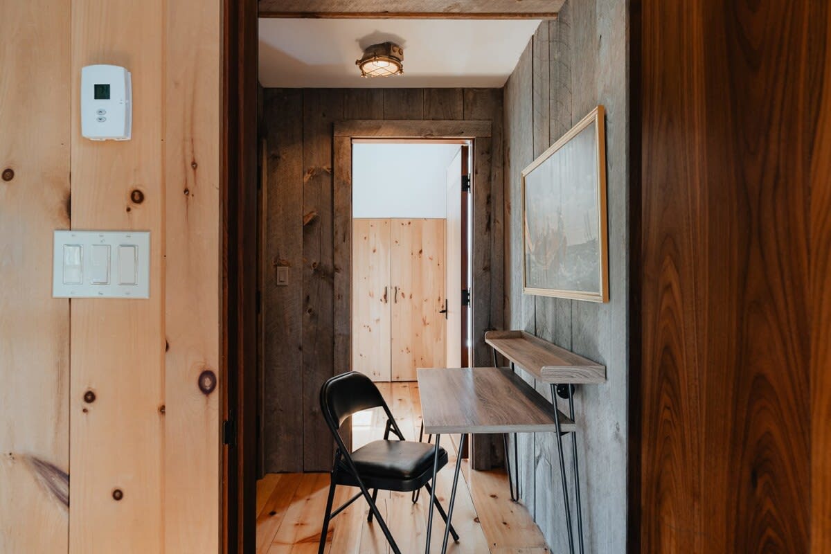 Small office nook or hallway with wood paneling, a simple wooden desk, a black folding chair, and a framed artwork on the wall, perfect for remote work.